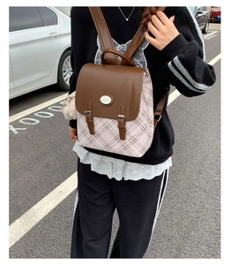 Detail of pink plaid backpack with brown leather flap and buckle closure in outdoor setting