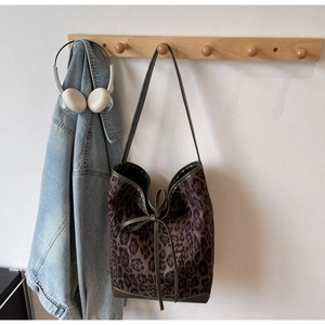 Détail du sac cabas léopard avec bordure en cuir vert et nœud sur un crochet en bois