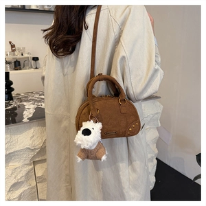 Detailed view of a brown suede bowling bag with gold hardware and plush dog charm