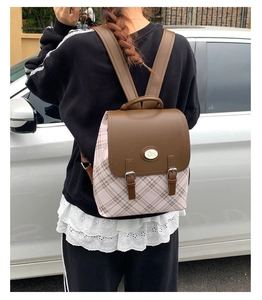 Outdoor shot of a pink plaid backpack with brown leather flap and metal buckle detail