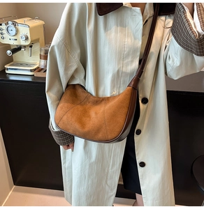Brown suede crescent moon bag worn over the shoulder in a cozy cafe setting