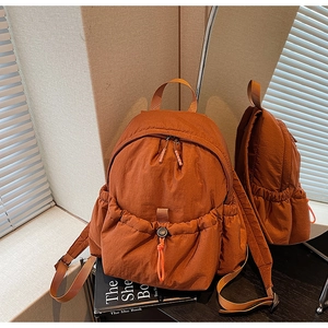 Detailed view of the terracotta nylon backpack with drawstring pockets in a warm aesthetic setting