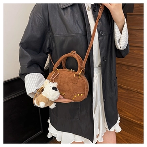 Close-up of brown suede bowling bag with gold studs and a white plush dog charm