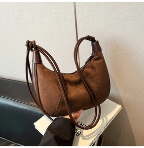 Detailed macro view of dark brown suede and leather stitching on the crescent bag