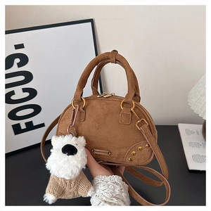Detail of a brown suede bowling bag featuring a white puppy charm and gold-tone metal hardware