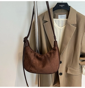 Detail of a brown suede hobo bag with leather trim hanging on a stainless steel rack