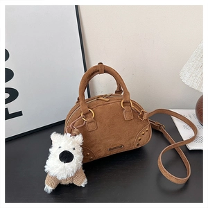 Detail of a brown suede Boston bag featuring gold hardware and a cute puppy plush charm