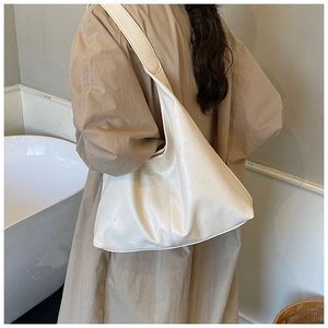 Minimalistische beige Hobo-Tasche aus Leder mit weicher Textur über der Schulter getragen