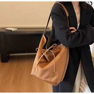 Détail d'un grand sac cabas en daim marron avec nœud décoratif porté par un mannequin