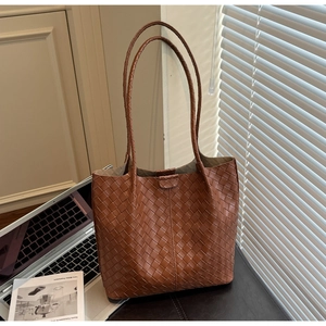 Close-up of brown woven tote bag with intricate leather texture on a minimalist office desk