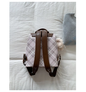 Detail of pink plaid backpack featuring brown faux leather straps and a plush ball charm