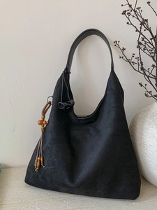 Grande borsa hobo in pelle scamosciata nera con nappine in legno su sfondo minimalista