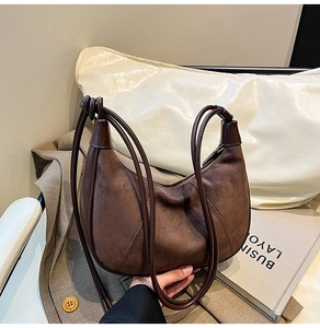 Detailed view of dark brown suede hobo bag with leather trim on a grey suit background