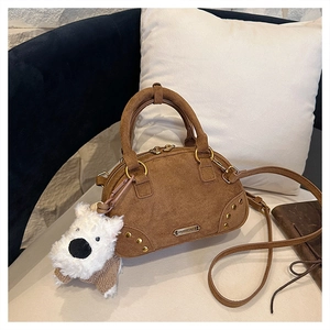 Detailed macro of brown suede bowling bag with golden rivets and cute white puppy charm