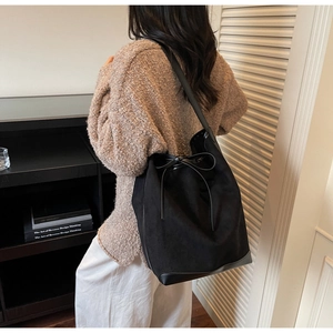 Détail d'un sac seau en daim noir mat avec cordon de serrage en cuir sur un pull beige chic