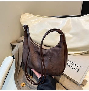Detail of dark brown suede half-moon bag featuring V-shaped stitching and leather straps