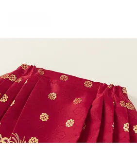 Detailed view of red satin fabric with gold flower embroidery and pleated waist design