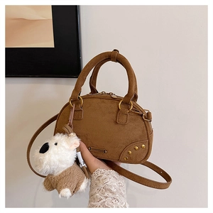 Detail of a brown suede bowling bag with golden rivets and a cute white puppy plush charm