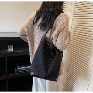 Détail du sac seau noir en daim mat avec bordure en cuir et nœud papillon élégant sur le côté