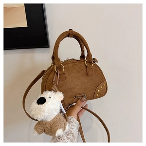Close-up of brown suede bowling bag featuring gold studs and a cute dog plush charm
