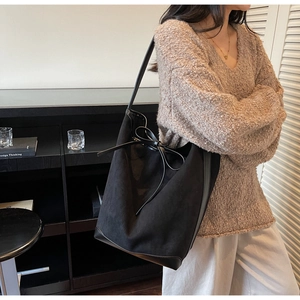 Détail du sac seau en daim noir avec un grand nœud décoratif et une base en cuir lisse noir