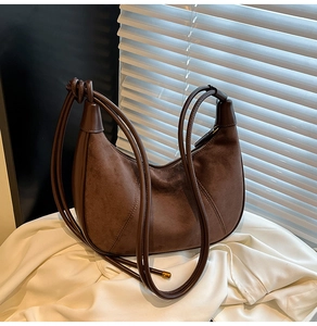 Detail of a brown suede crescent bag with leather trim and knotted shoulder strap