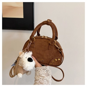Close-up of brown suede bowling bag featuring golden rivets and a cute puppy plush charm