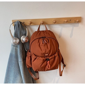 Close-up of caramel nylon backpack with drawstring pocket hanging on a wooden hook
