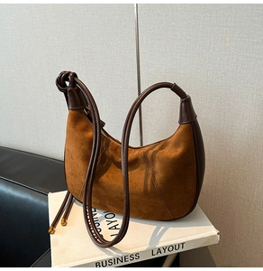 Detail of suede hobo bag with leather stitching, decorative tassels and zip closure