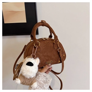 Detail of brown suede handbag featuring gold hardware and a cute white puppy plush charm