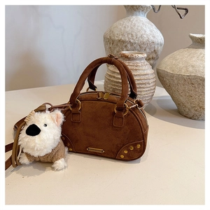 Brown faux suede bowling bag featuring gold rivets and a cute plush dog charm on a desk