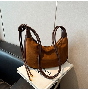 Detailed view of brown suede hobo bag with knotted leather straps on white books