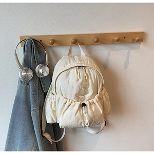 Detail of a minimalist beige nylon backpack with drawstring front pocket and textured fabric