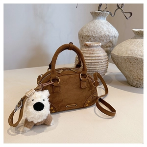 Detail view of brown suede bowling bag with golden studs and a cute teddy bear charm