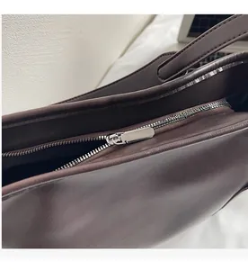 Close-up of a smooth silver metal zipper on a dark brown textured leather tote bag