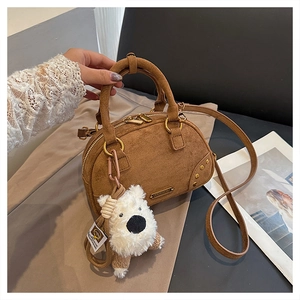 Close-up of brown suede Boston bag featuring golden hardware and a white plush bear charm