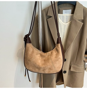 Detailed view of brown suede crescent bag with leather strap and knot on a fashion stand