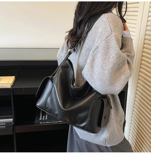 Detail view of a black large synthetic leather tote bag with side flap pocket and long strap