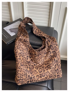 Close-up of leopard print tote bag fabric and wide shoulder strap on dark leather surface