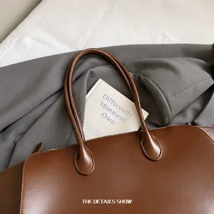 Detailansicht der braunen Leder-Tote-Bag mit weichem Rundgriff auf grauem Mantel