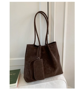 Detail of dark brown suede tote bag with small attached pouch on a white sofa