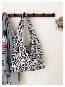 Close-up of zebra pattern canvas tote bag hanging on wooden hook with denim jacket