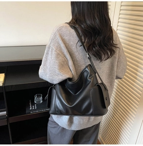 Detailed view of black leather tote bag featuring a side pocket and adjustable shoulder strap