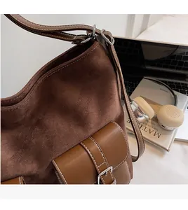 Close-up of brown suede shoulder bag with contrast stitching and adjustable strap details