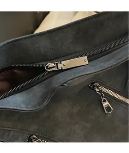 Détail des fermetures éclair métalliques polies et des curseurs sur un cabas en daim gris