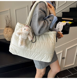 Close-up of off-white quilted tote bag with wide shoulder strap and plush rabbit charm