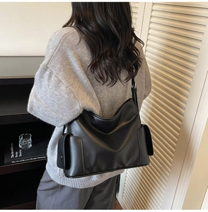 Detail view of large black leather tote bag with side flap pockets and adjustable strap