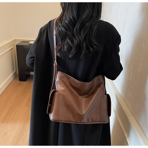 Detail view of a vintage brown leather tote bag with side pockets on a model's shoulder