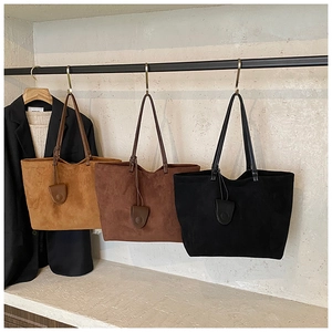 Detailed close-up of suede tote bags in mustard, brown, and black hanging on a retail display