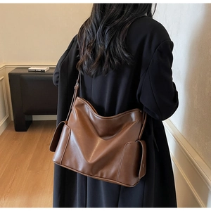 Brown leather tote bag featuring side flap pockets and adjustable shoulder strap